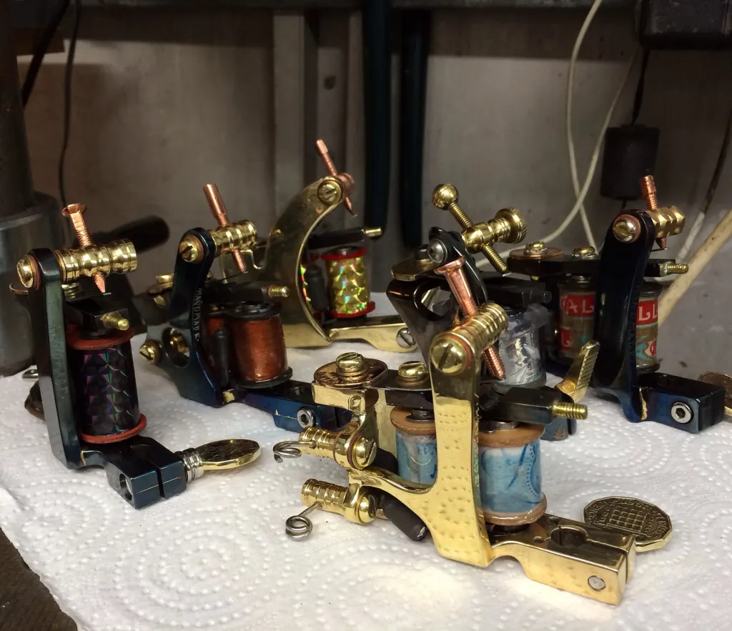 Handmade vintage-style coil tattoo machines laid out on a table