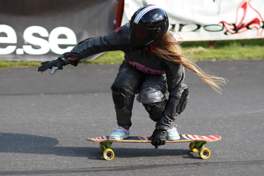 A downhill longboard rider in a black helmet and leathers crouches low on a skateboard on an asphalt race course at the 2014 Taberg Downhill Challenge in Sweden
