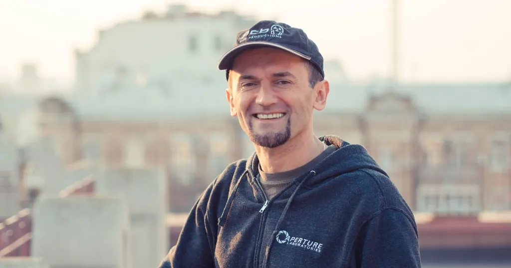 4A Games founder Andrew Prokhorov, in a dark cap and hooded jacket, smiling on a rooftop with city buildings behind him