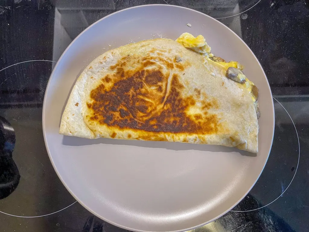 A breakfast quesadilla filled with egg, cheese and mushroom, cut into wedges on a plate