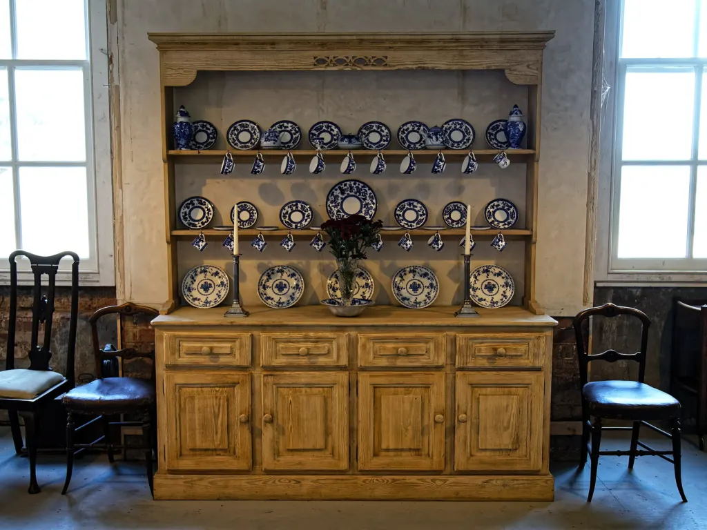 A traditional wooden kitchen dresser with open shelves holding tableware in the housekeeper's room at Copped Hall, Essex, England