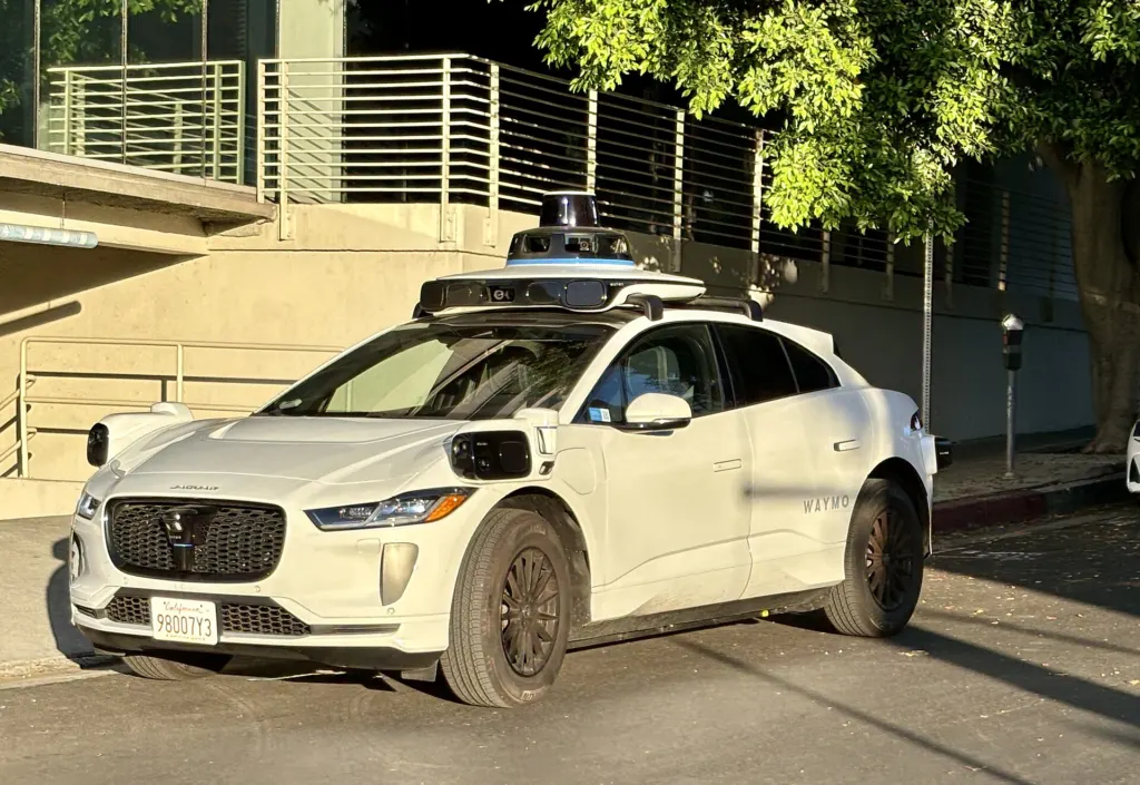 A Waymo driverless Jaguar I-Pace robotaxi with roof-mounted sensors on a street in Century City, Los Angeles, in August 2024