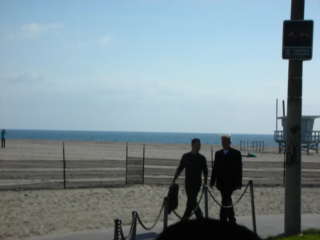 Mark Harmon and Chris O'Donnell walking along a beachfront path, with the ocean and a lifeguard tower behind them, during NCIS location filming on March 8, 2009