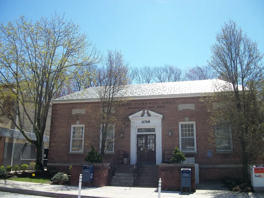 Brick front of the United States Post Office in Northport, New York, with an American flag on a pole outside