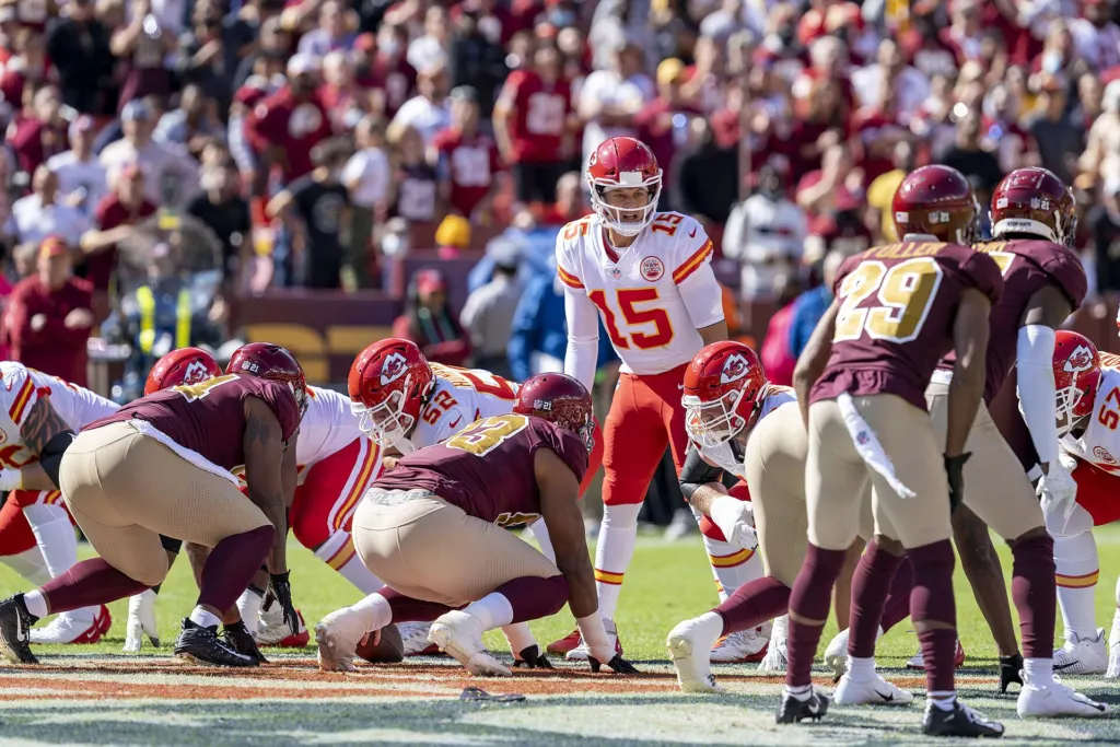 Patrick Mahomes in a red Kansas City Chiefs uniform crouched behind the center, getting ready to take the snap