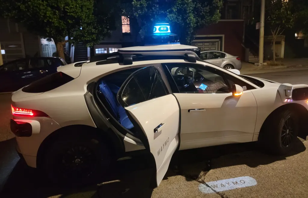 A white Waymo Jaguar I-Pace robotaxi with roof sensors on a street at night