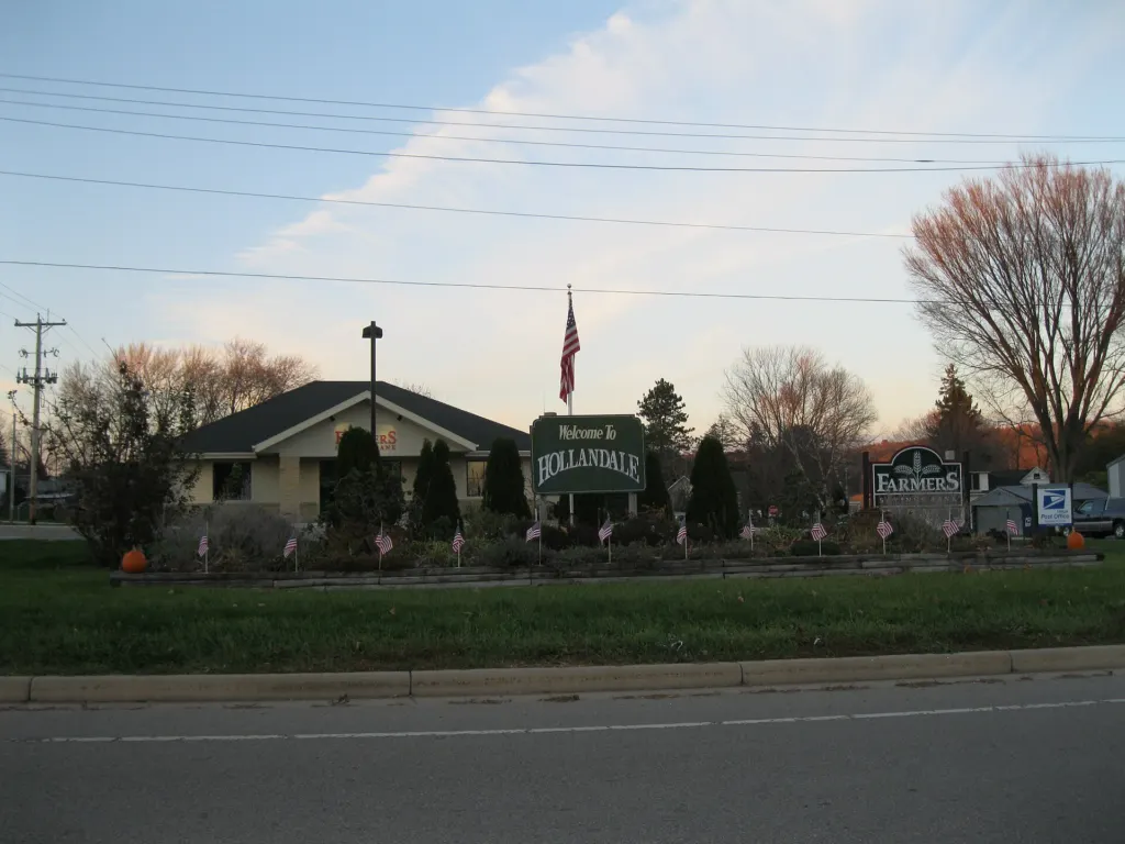 A small bank building in Hollandale, Wisconsin, with a Welcome To Hollandale sign on the lawn in front