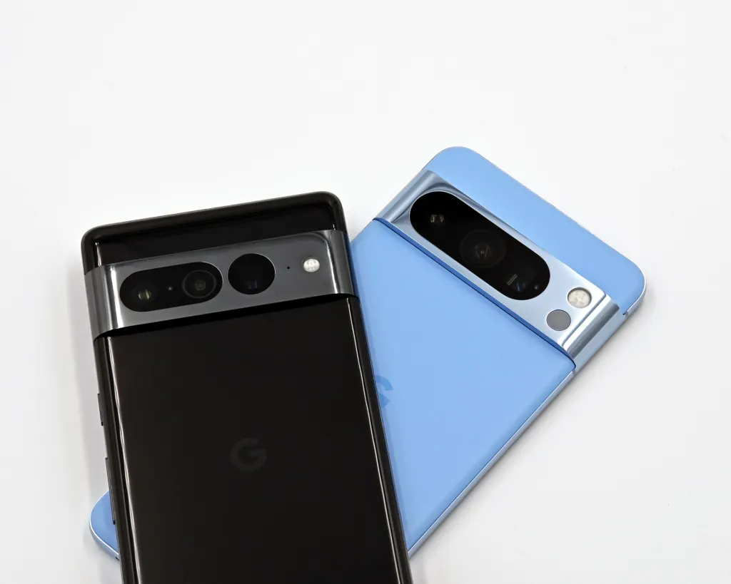 Two Android phones, a black Google Pixel 7 Pro and a light blue Pixel 8 Pro, lying face down on a white surface