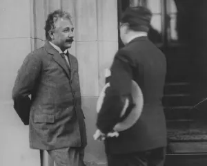 Albert Einstein in a tweed suit, hands behind his back, standing beside a stone doorway and talking with a man holding a straw hat, in Buenos Aires in 1925