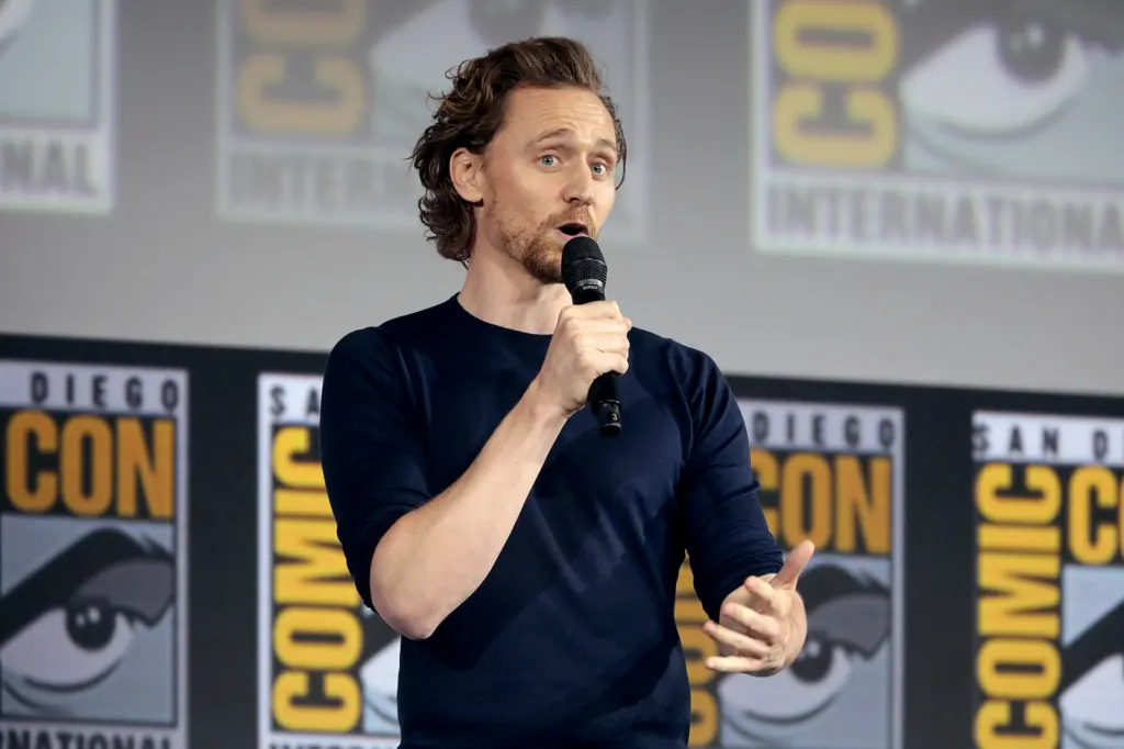 Tom Hiddleston speaking into a microphone on stage at San Diego Comic-Con in 2019 during a panel for the Loki series