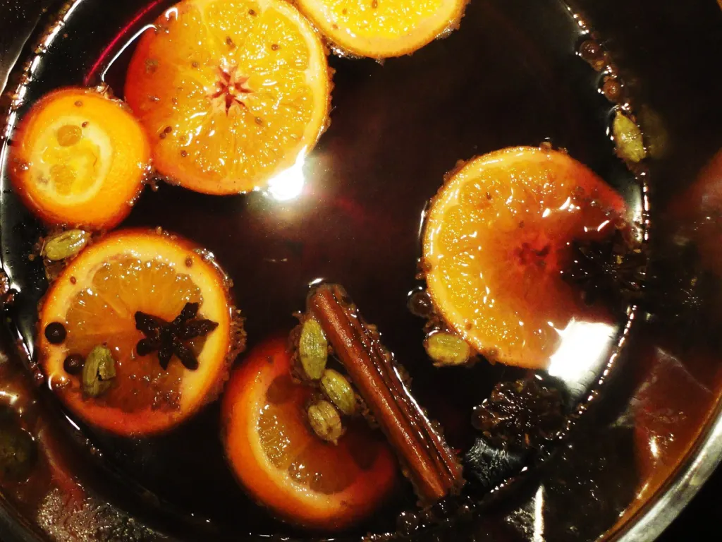 A pot of dark liquid simmering with orange slices, cinnamon sticks and whole spices