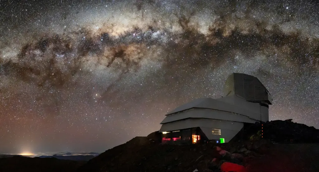 The Vera C. Rubin Observatory dome on a Chilean mountaintop at night under the bright band and dark dust lanes of the Milky Way